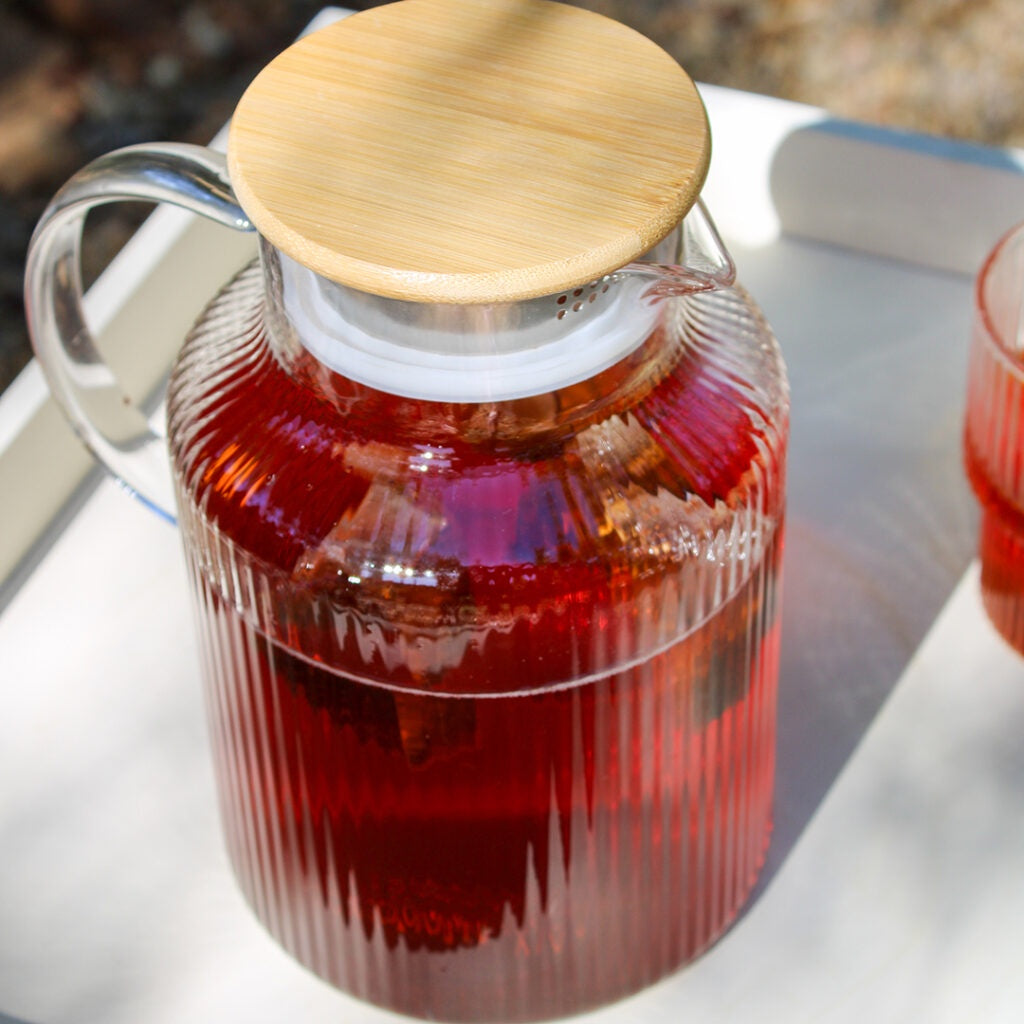 Glass jug with wooden lid filled with red tea on a white surface