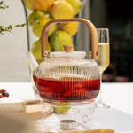 Load image into Gallery viewer, A clear glass teapot with a bamboo handle and a removable strainer, filled with tea on a table.
