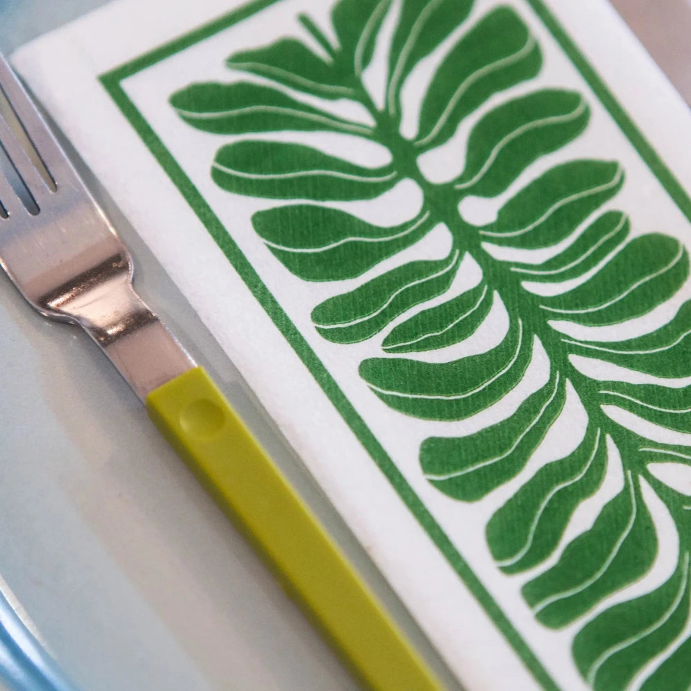 Napkin with green leaf pattern, fork, and knife on a white surface