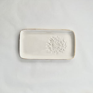A white ceramic slate with a king protea embossed on the right hand side and gold detailing on the rim. 