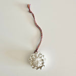 Load image into Gallery viewer, White floral decoration on a braided cord against a light background

