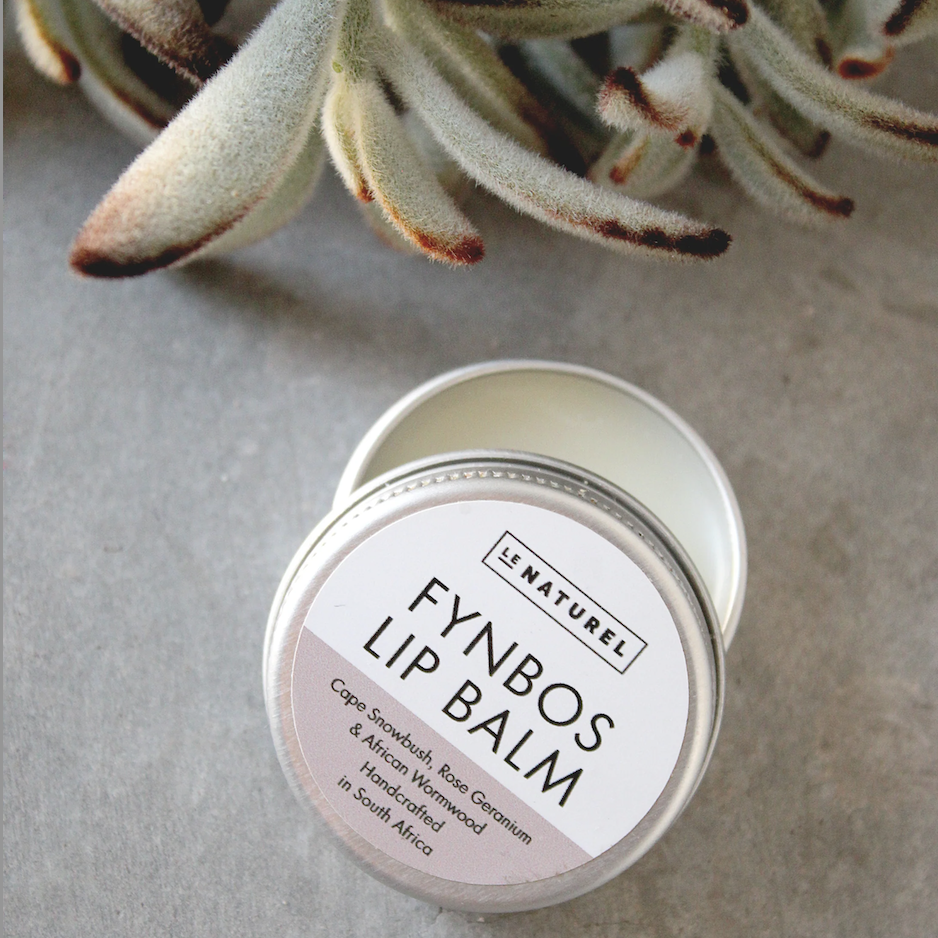 A tin container of Le Naturel Fynbos Lip Balm with a label showing the product name and some decorative plant in the background.