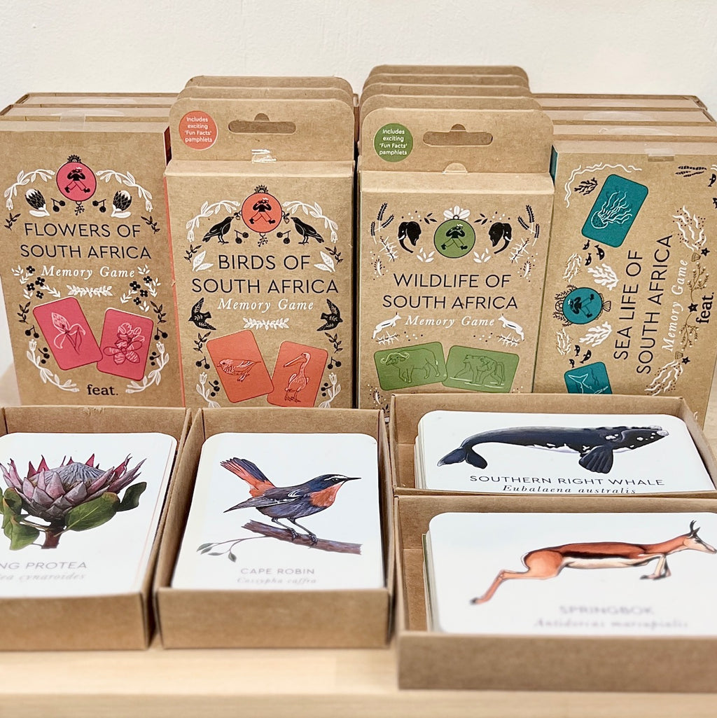 A display of boxed games with samples open in front of them. Each sample is displaying either a king protea, cape robin bird, southern right whale or springbok with their common and scientific names.