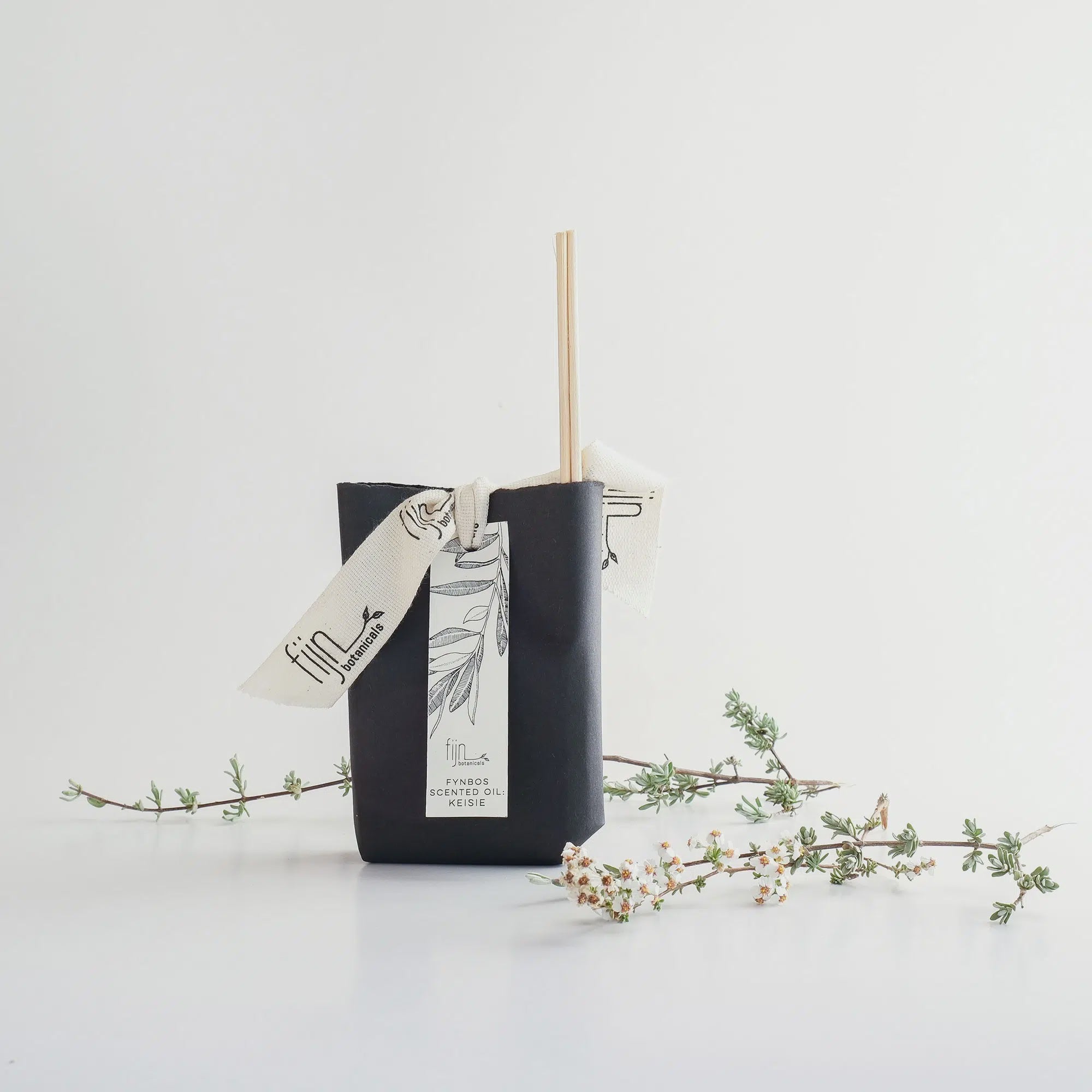 Black reed diffuser with a decorative ribbon on a white background