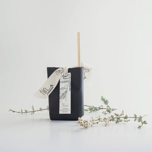 Black reed diffuser with a decorative ribbon on a white background