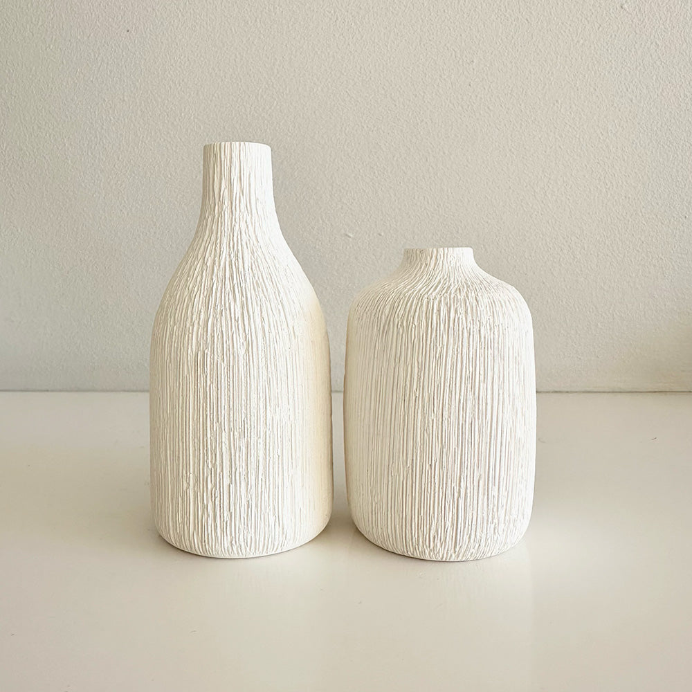 Two textured white vases on a light surface with a neutral background