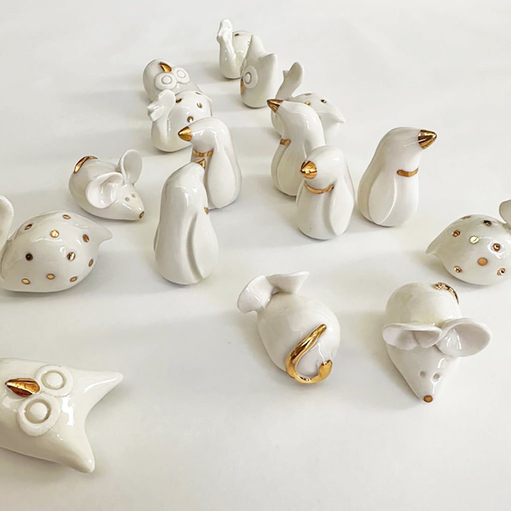 A collection of handcrafted ceramic animals with gold accents, including birds and rabbits, displayed on a white background.