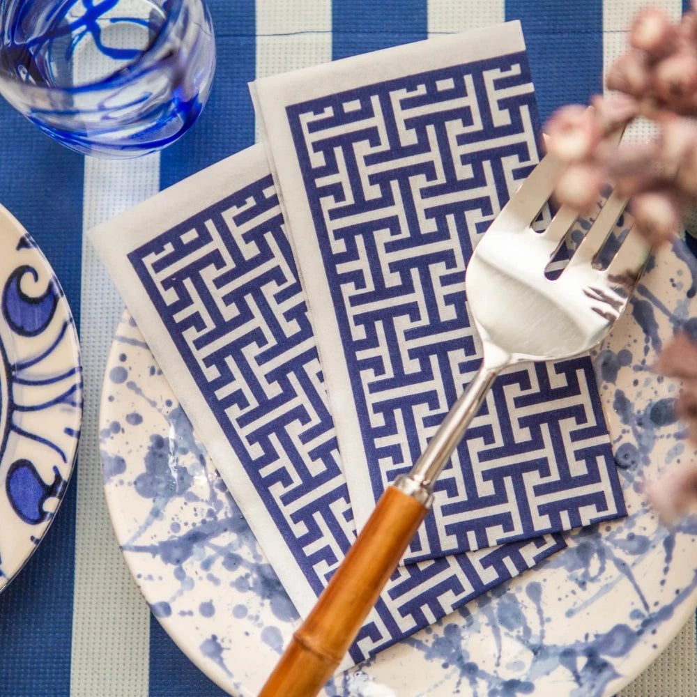 Table setting with blue and white patterned plates, napkins, and cutlery on a striped tablecloth.