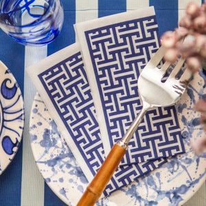 Table setting with blue and white patterned plates, napkins, and cutlery on a striped tablecloth.
