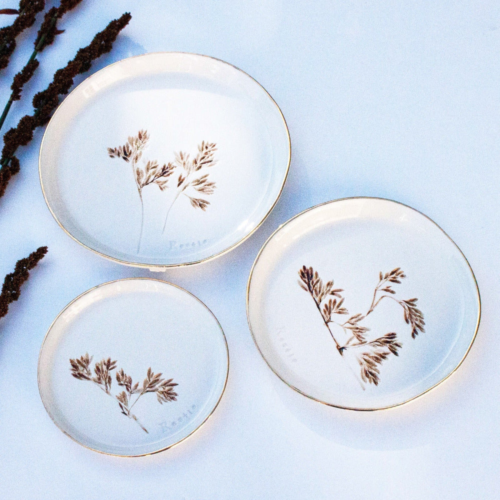 Three ceramic plates with gold rims and botanical designs on a light blue background