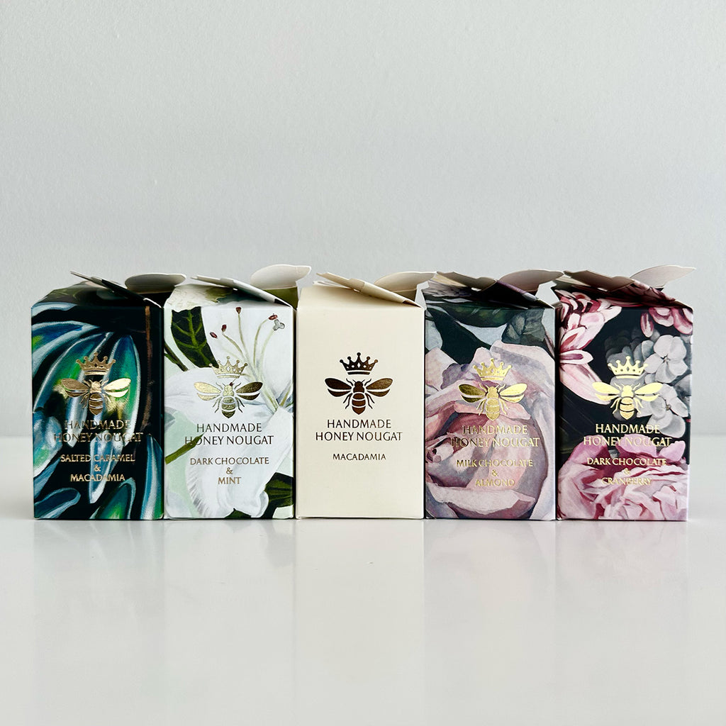 Five boxes of handmade honey nougat with floral and bee designs on a light gray background.
