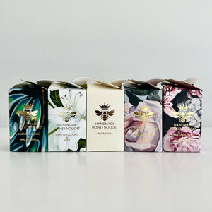 Five boxes of handmade honey nougat with floral and bee designs on a light gray background.