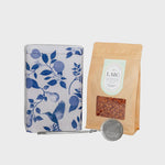 Load image into Gallery viewer, Tea set with floral-patterned tin, brown paper bag with tea leaves, and silver tea spoon on a light gray background
