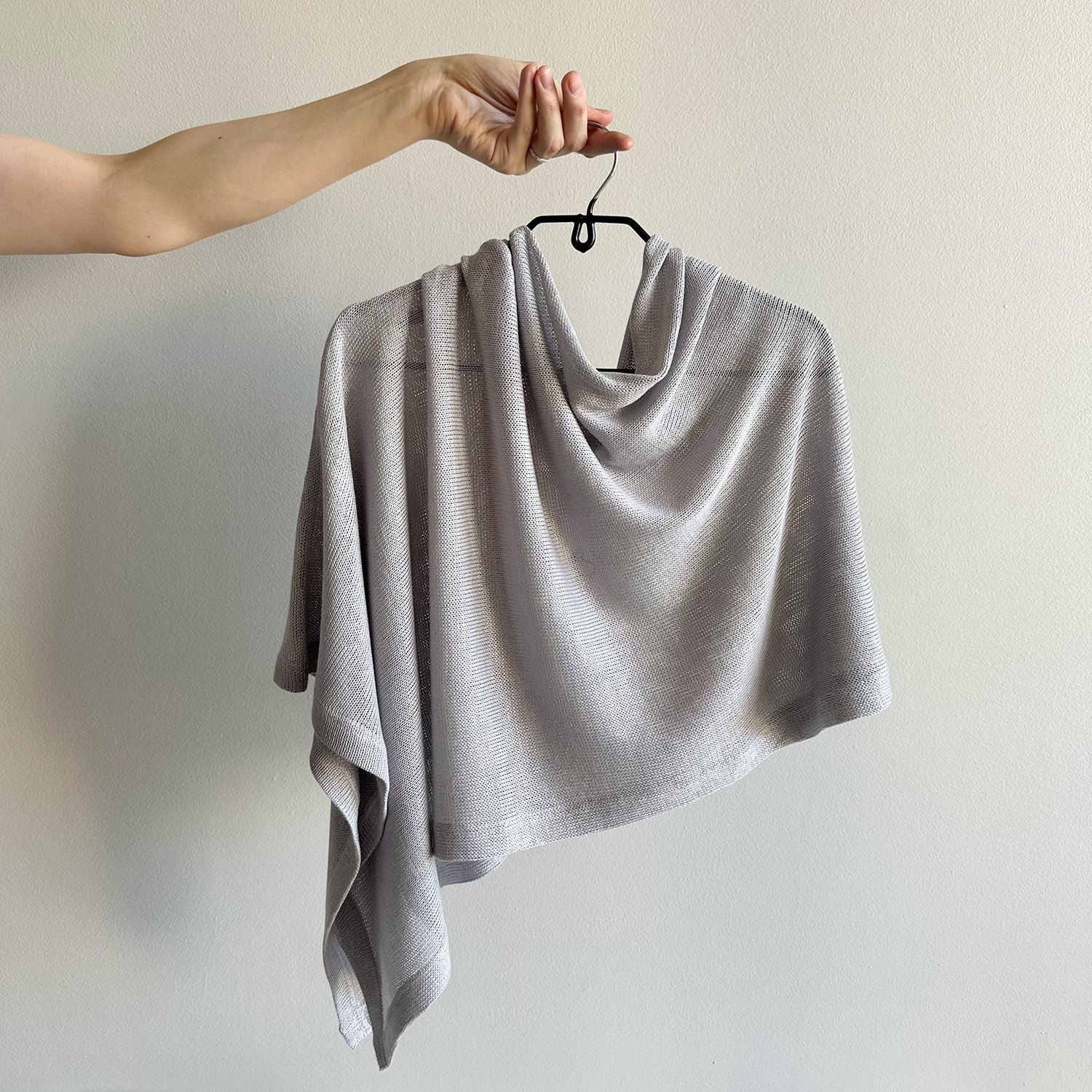 Gray knitted shawl on a hanger against a plain background