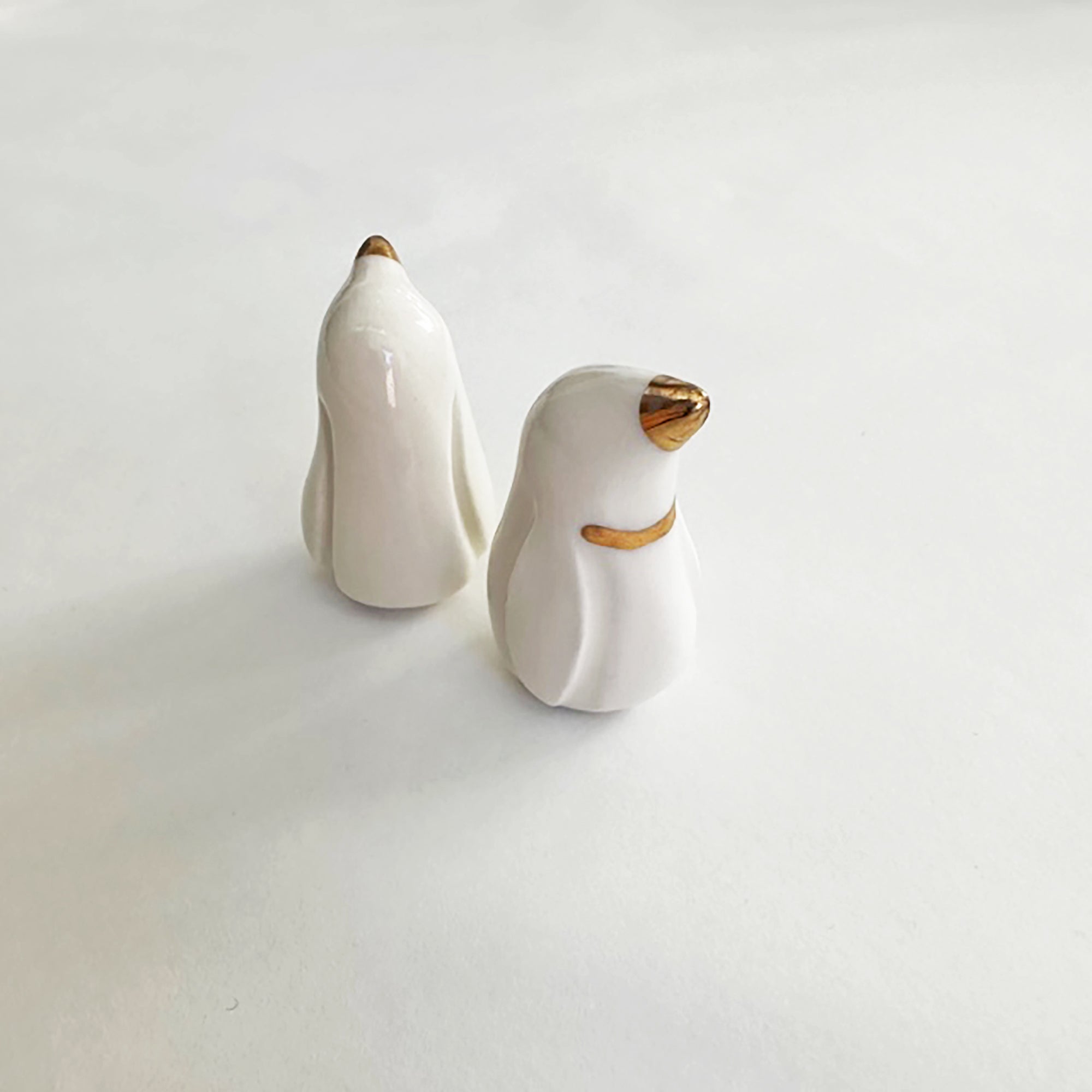 A pair of handcrafted ceramic penguins with gold accents displayed on a white background.
