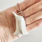 Load image into Gallery viewer, Hand holding a small white ceramic penguin ornament with a string
