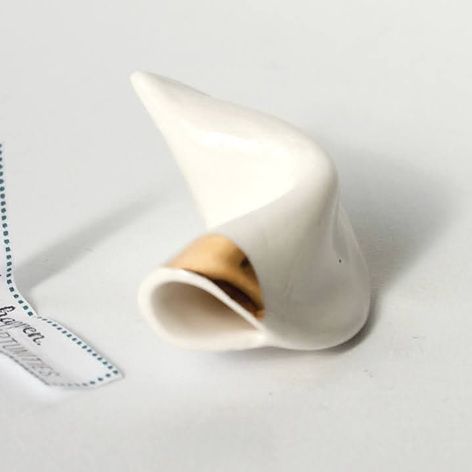 White ceramic fortune cookie with 18 carat gold accent on a light gray background