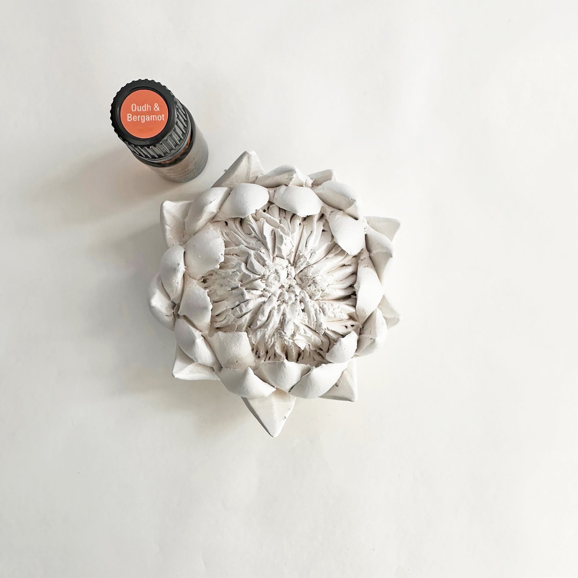 A bisquewear ceramic protea sculpture alongside a frangrance oil bottle on a white background.