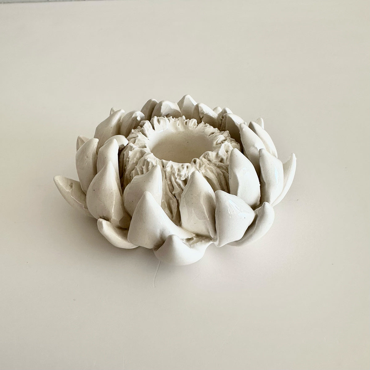 White ceramic protea-shaped candle holder on a light beige background