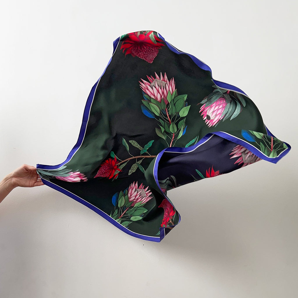 Floral patterned silk scarf held by a hand on a plain background