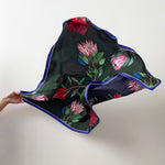 Load image into Gallery viewer, Floral patterned silk scarf held by a hand on a plain background
