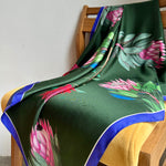 Load image into Gallery viewer, A close-up image of a reversible silk scarf with colourful protea illustrations draped on a chair. 
