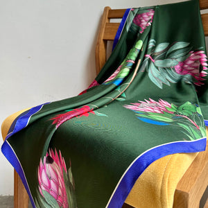 A close-up image of a reversible silk scarf with colourful protea illustrations draped on a chair. 
