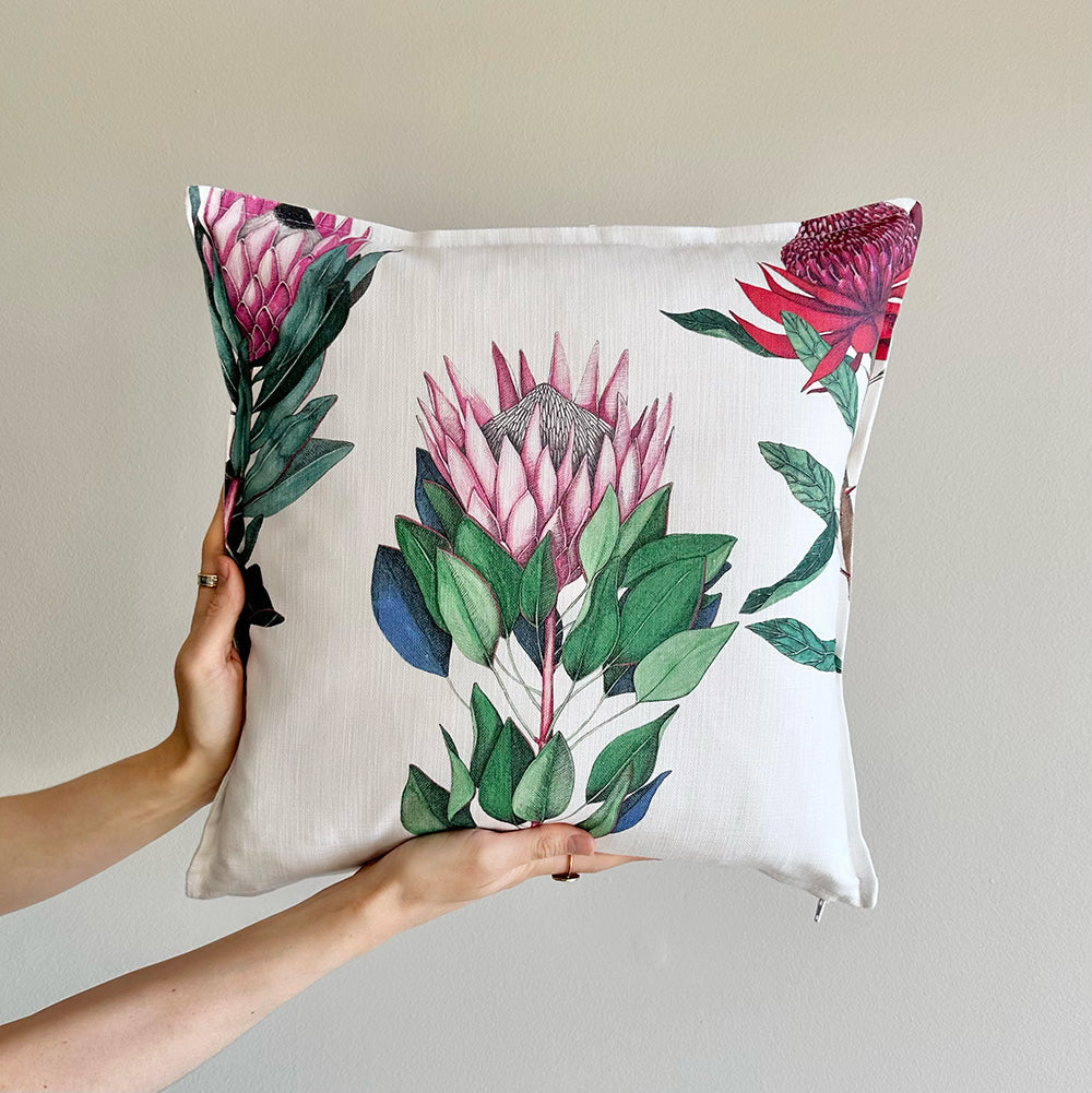 Protea floral-patterned pillow held by a hand against a neutral background