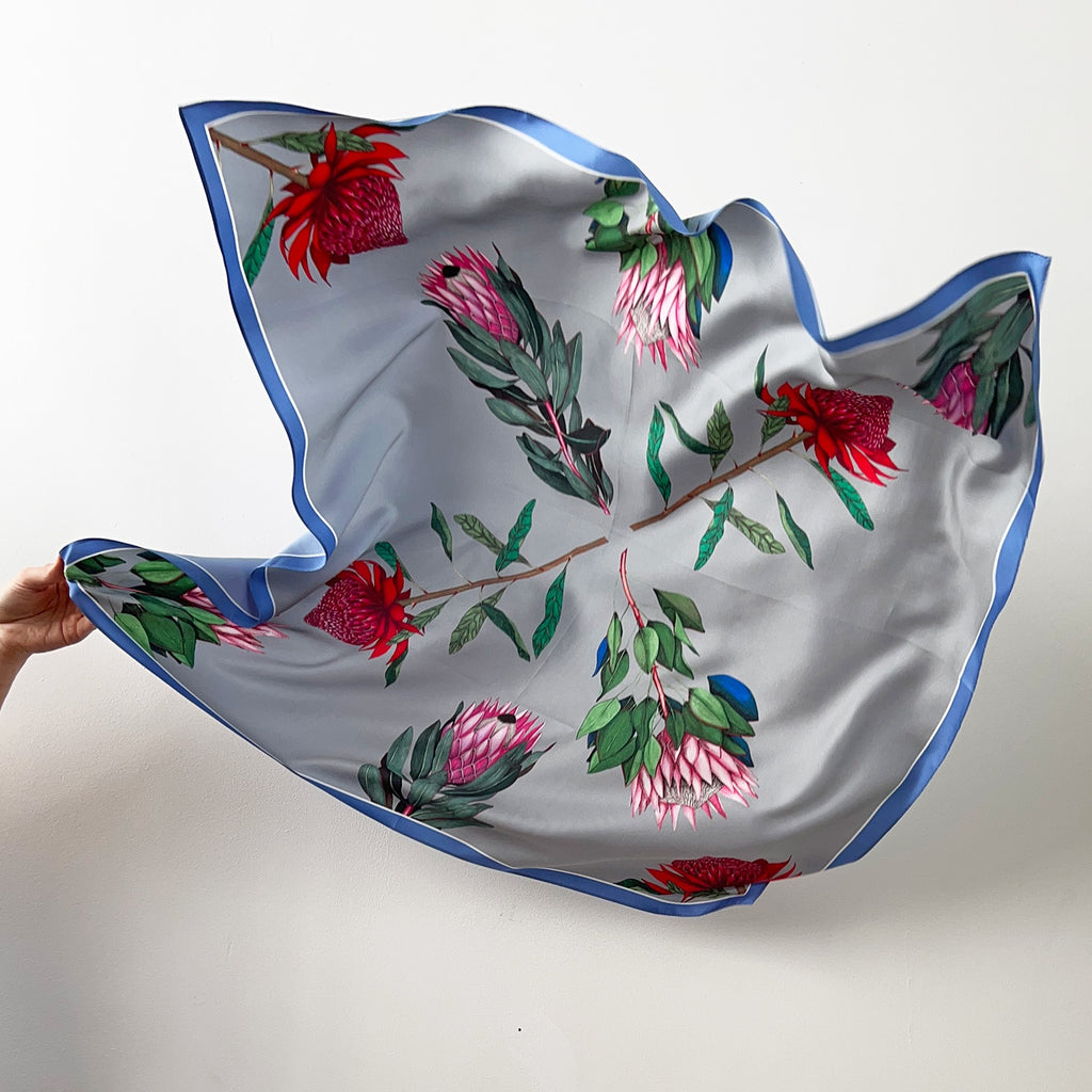 Floral patterned silk scarf held by a hand on a white background
