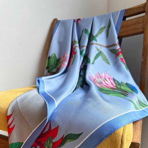 A close-up image of a reversible silk scarf with colourful protea illustrations draped on a chair. 