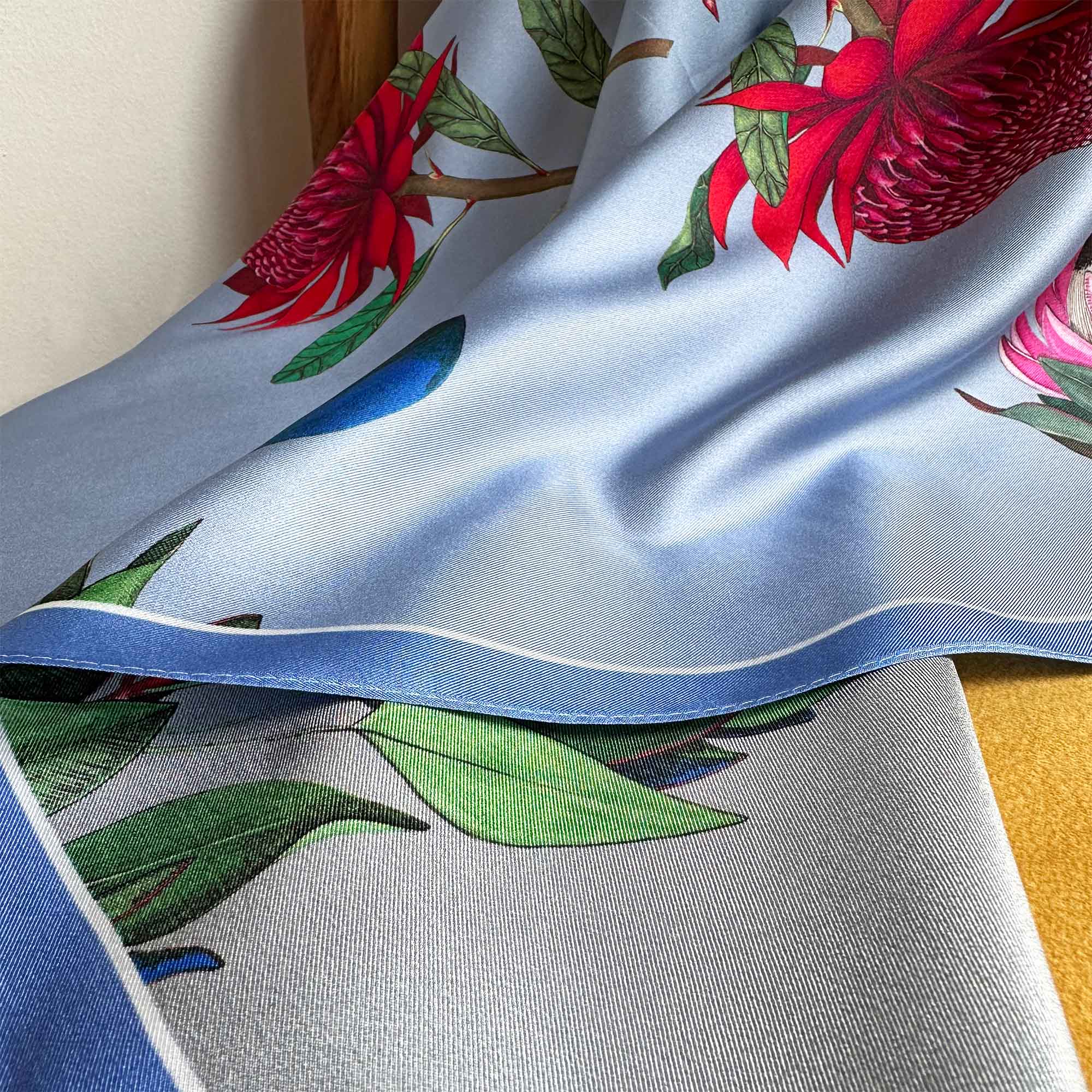 A close-up image of a reversible silk scarf with colourful protea illustrations draped on a chair. 