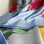 Load image into Gallery viewer, A close-up image of a reversible silk scarf with colourful protea illustrations draped on a chair. 
