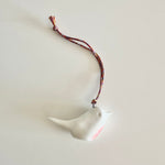 Load image into Gallery viewer, White ceramic bird ornament with a red accent on a string against a light gray background
