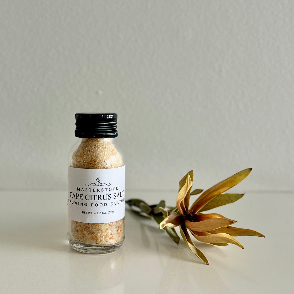 Bottle of Cape Citrus Salt with a decorative plant on a neutral background