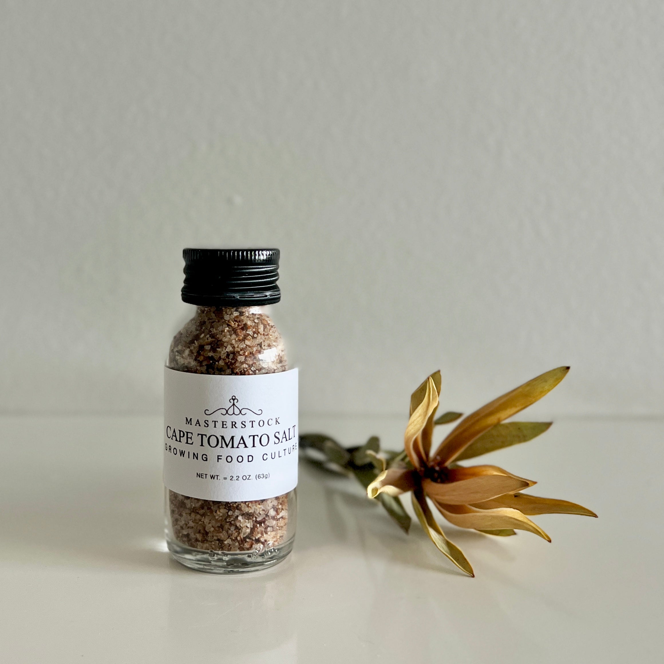 Bottle of Cape Tomato Salt with a decorative flower on a neutral background