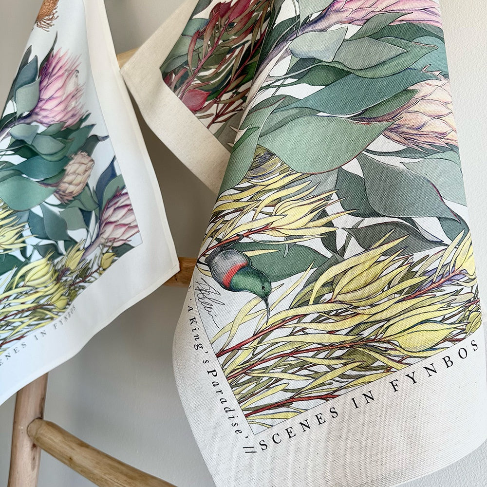 Tea towels with south african nature-themed designs on a wooden chair.