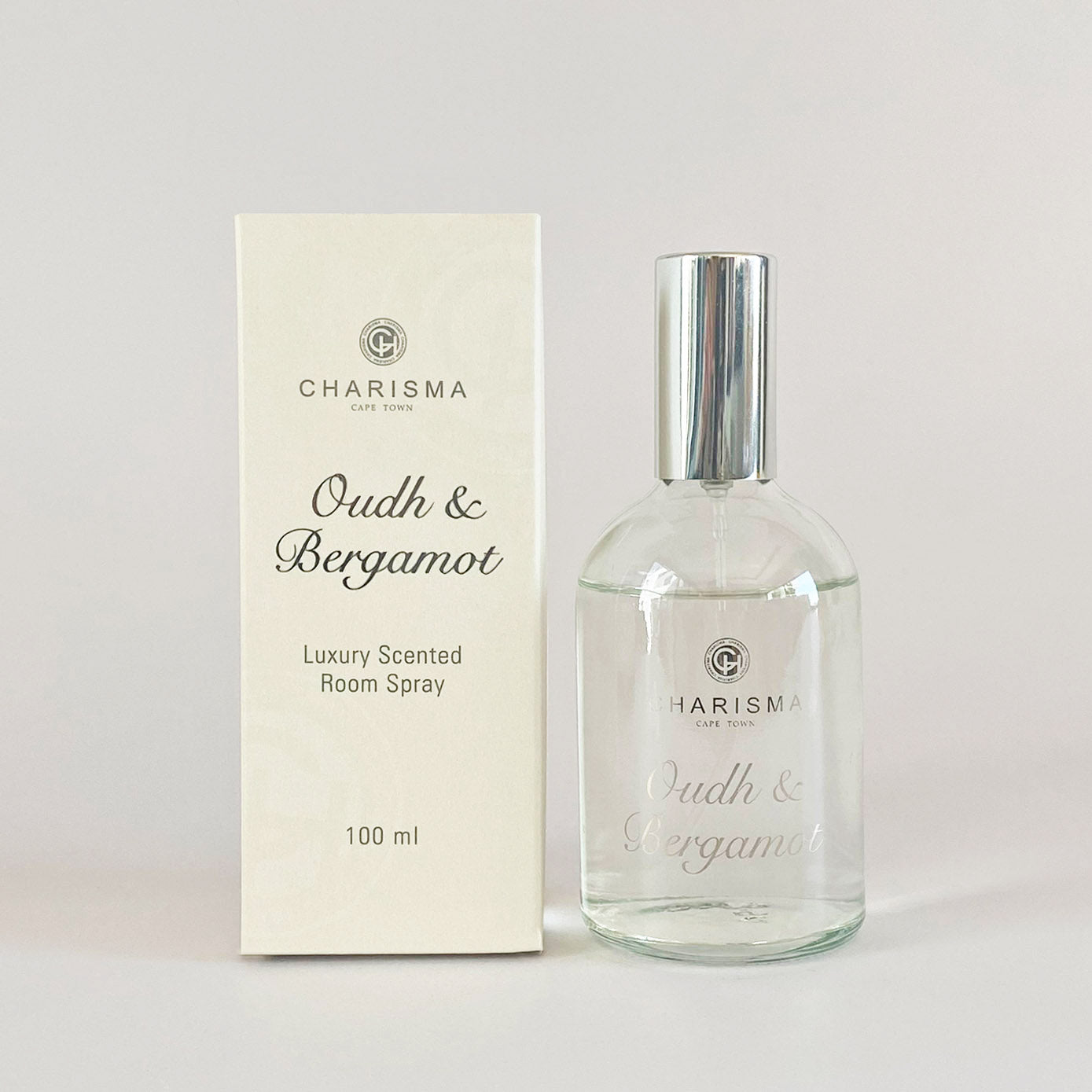 a glass bottle of clear room spray with silver lid standing alongside a cream box with 'OUDH & BERGAMOT LUXURY SCENTED ROOM SPRAY' in silver foiling. 