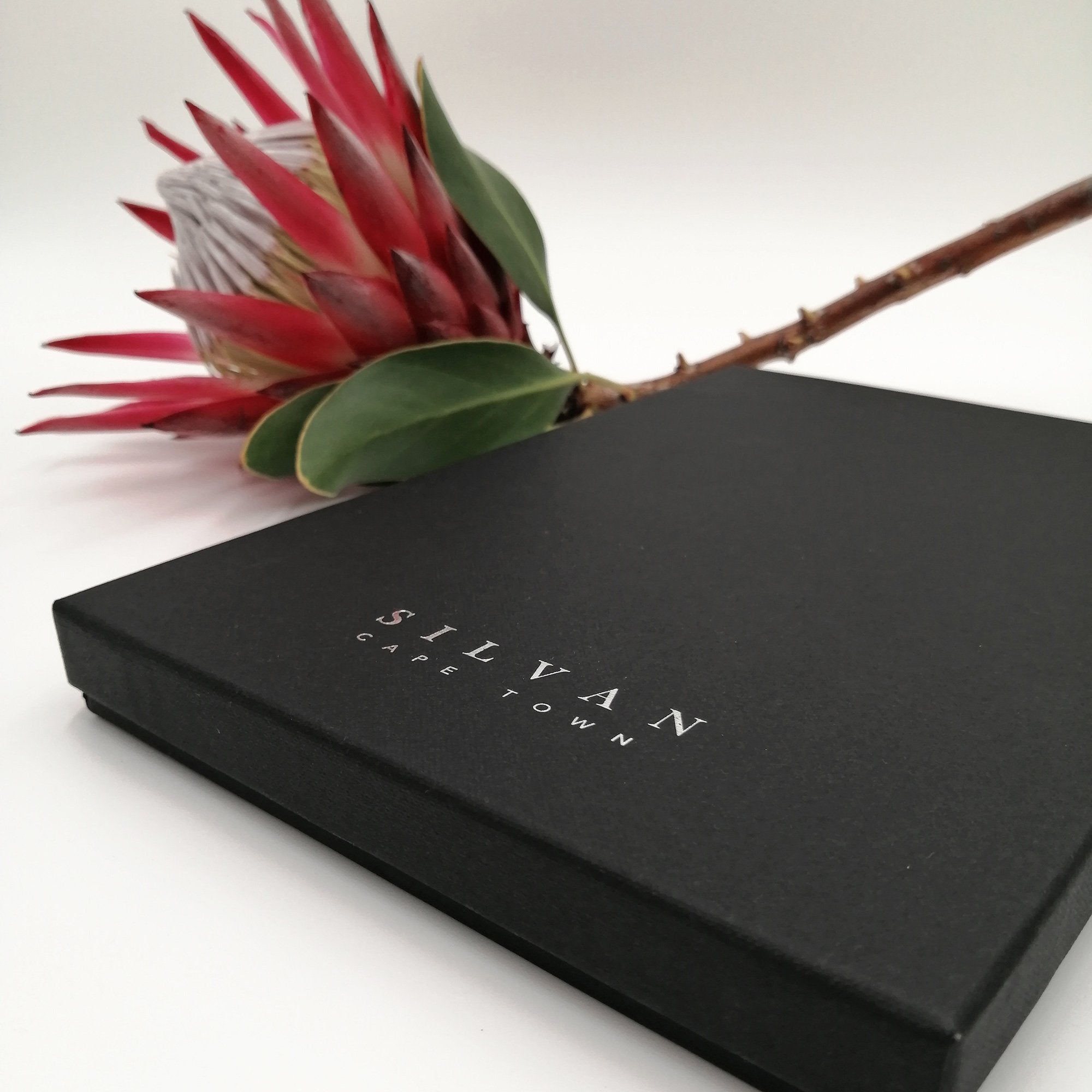 A black scarf box with silver foiled embossed branding.