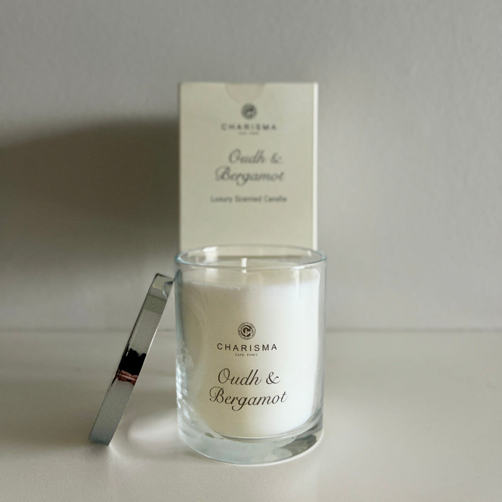 Glass candle with 'Oud & Bergamot' fragrance and branded packaging on a neutral background