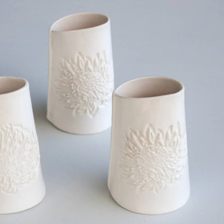 Three white ceramic dressing jugs with protea embossed design on a gray background