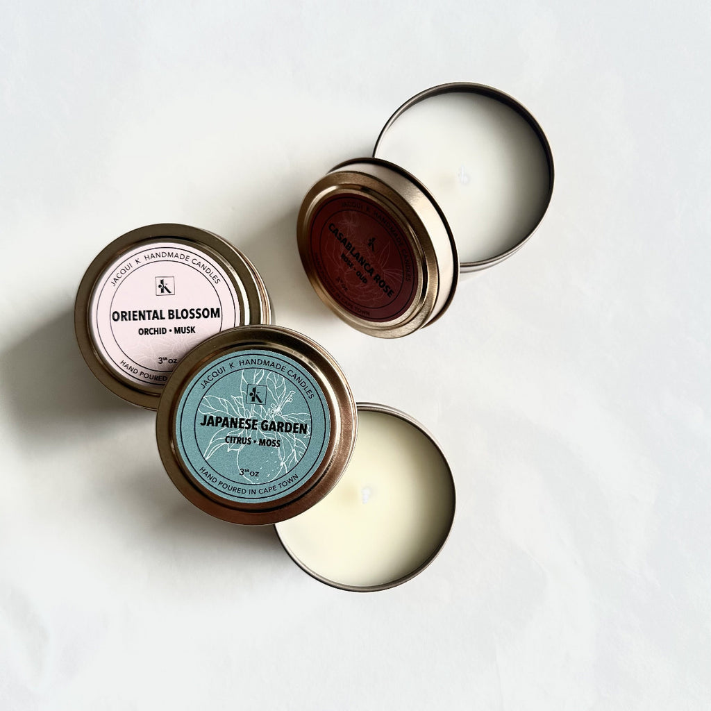 Three small candles in tins with visible labels on a white background