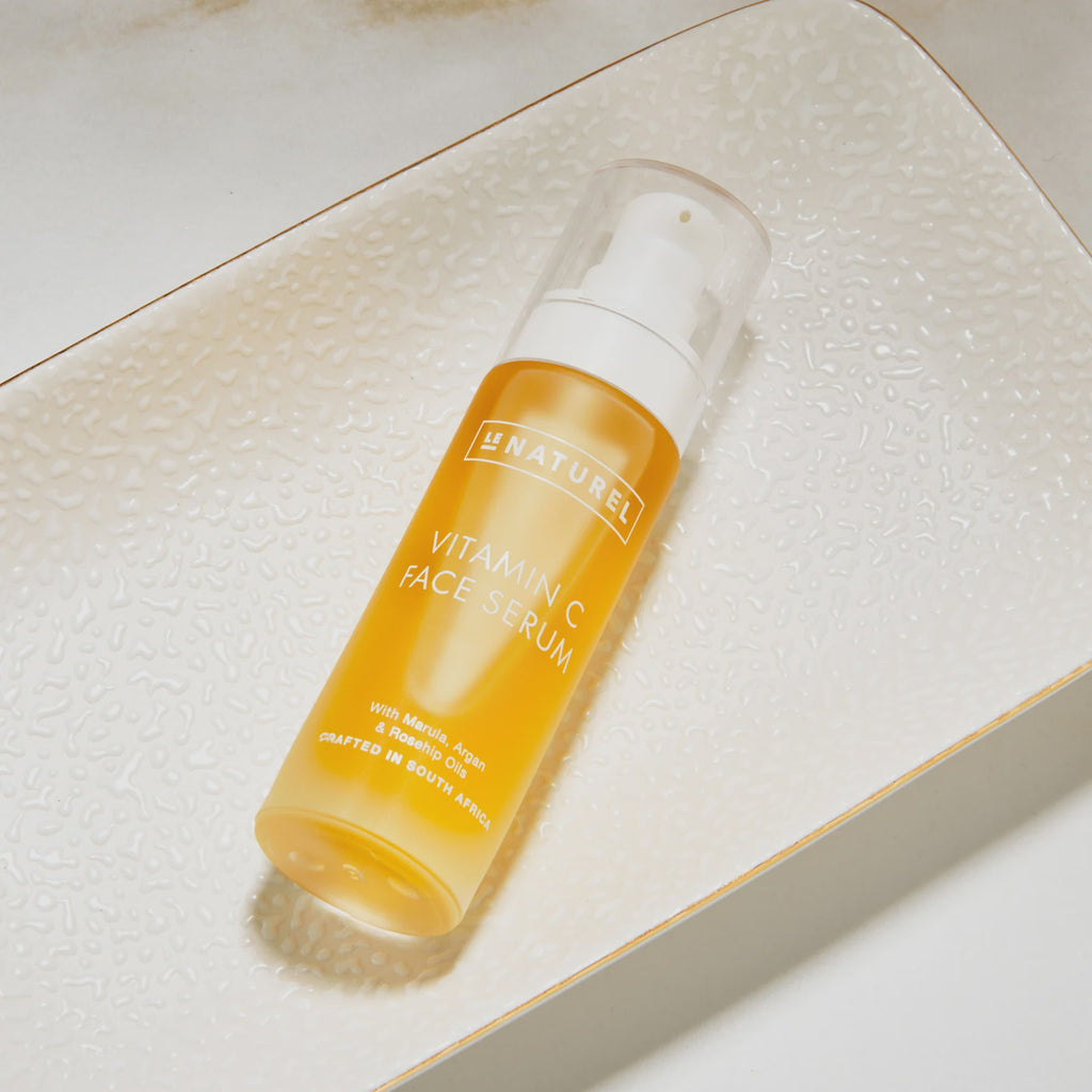 A bottle of Vitamin C Serum with a yellow tint, placed on a textured surface.