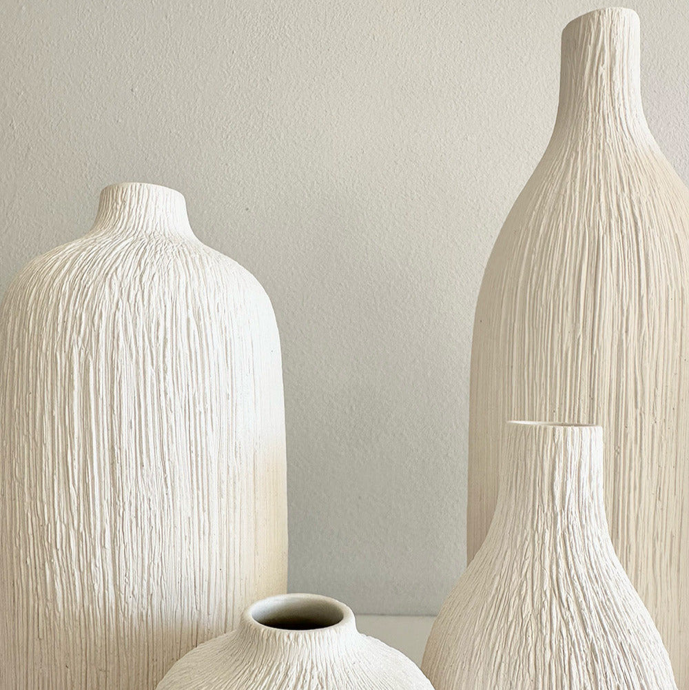 Set of four textured white vases against a neutral background