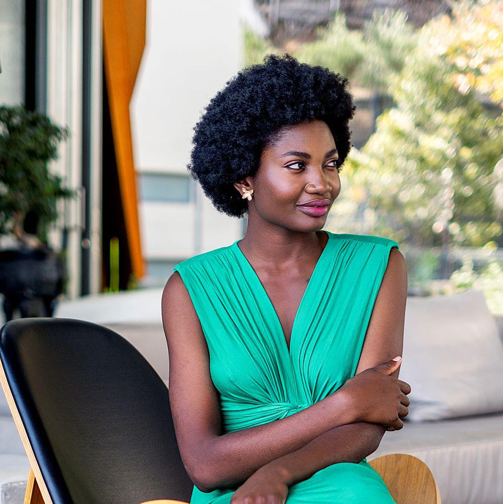 Woman in a green dress wearing bronze earrings sitting outdoors with blurred background
