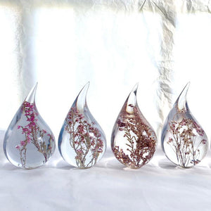Four resin drops sculpted in a teardrop shape with purple Erica fynbos flowers embedded, positioned on a textured surface with a white background.