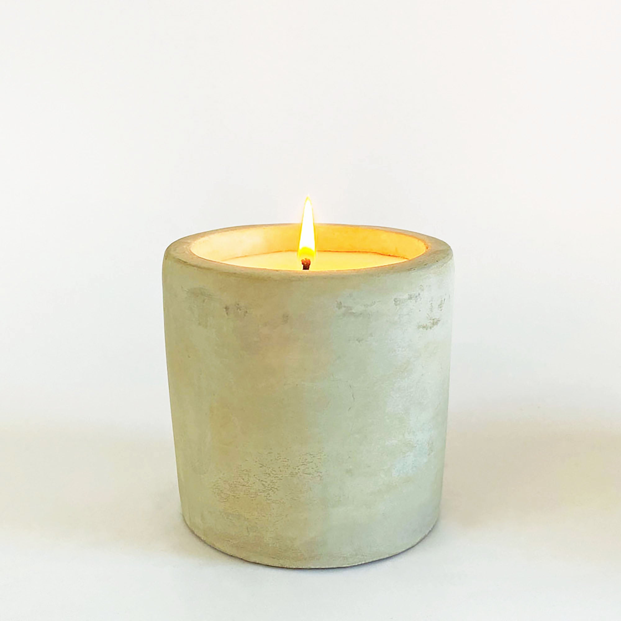 A single wick candle with a lemongrass scent, housed in a raw cement container with a visible wick and a small flame.
