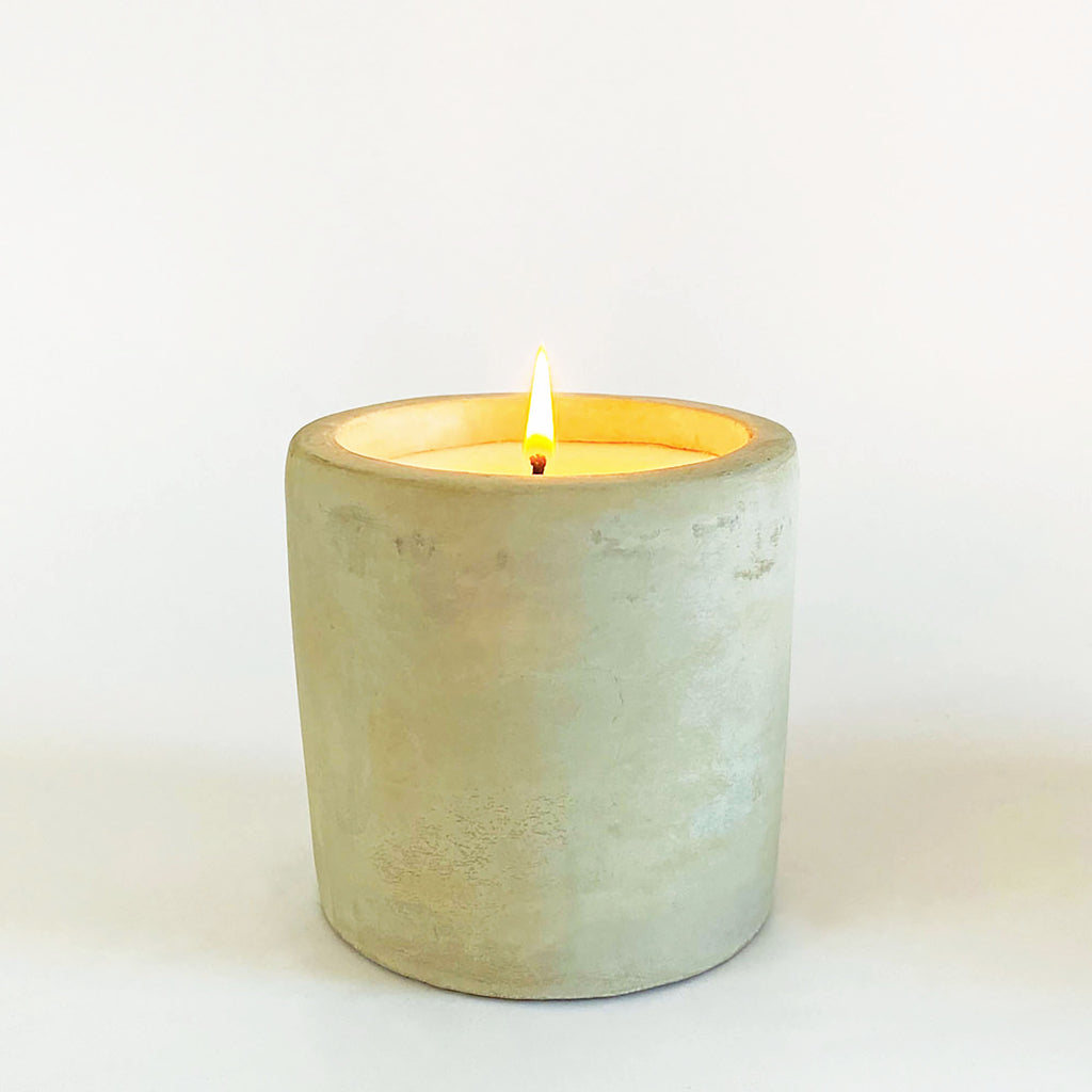 A single wick candle with a lemongrass scent, housed in a raw cement container with a visible wick and a small flame.