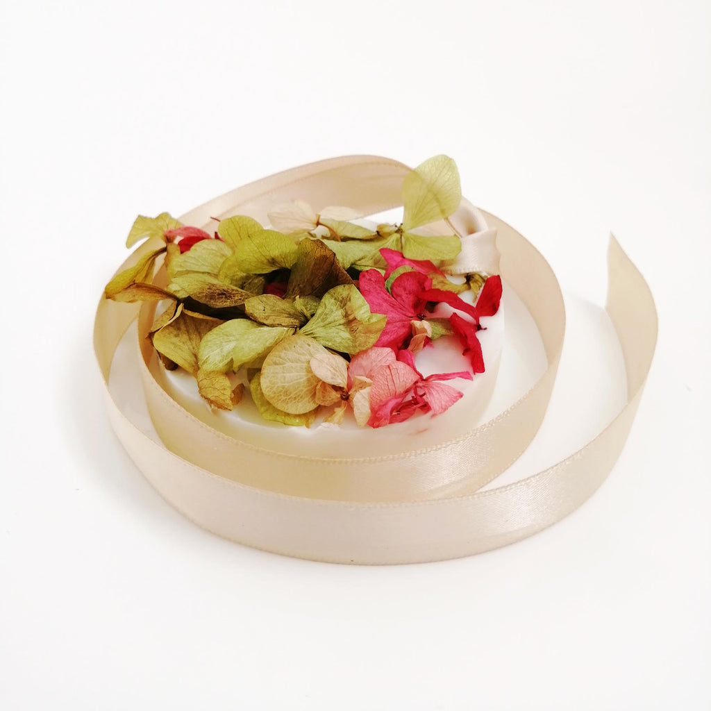 A beige wax tablet with pomegranate, bergamot, and patchouli scent, accompanied by dried petals, displayed on a white background.