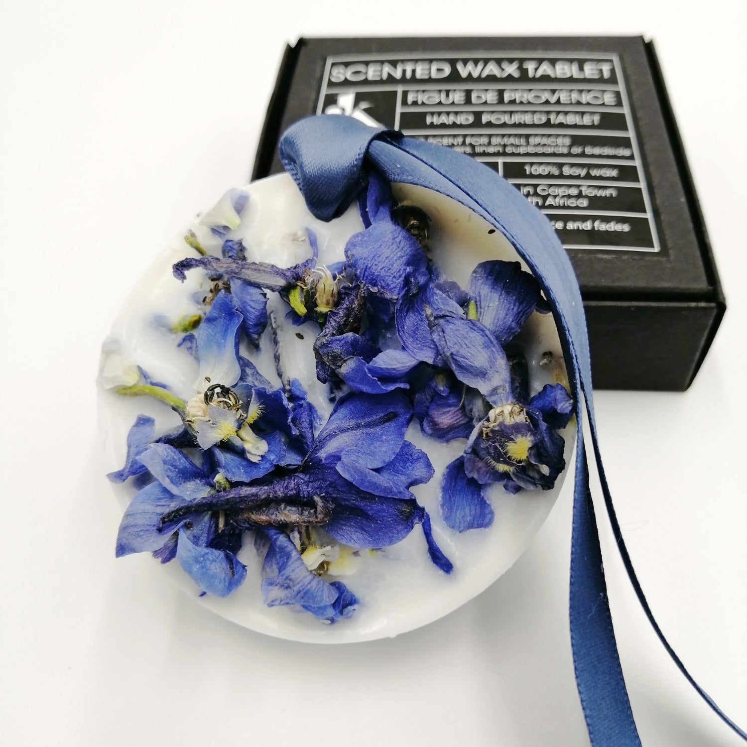 Decorative wax tablet with blue petals and a blue ribbon, with a box labeled 'Scented Wax Tablet Figue de Provence' in the background.