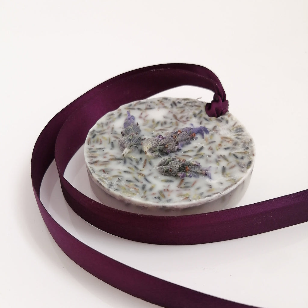 A round scented wax tablet with a lavender fragrance, adorned with dried lavender sprigs, encased in a clear wax layer, and attached to a purple ribbon.